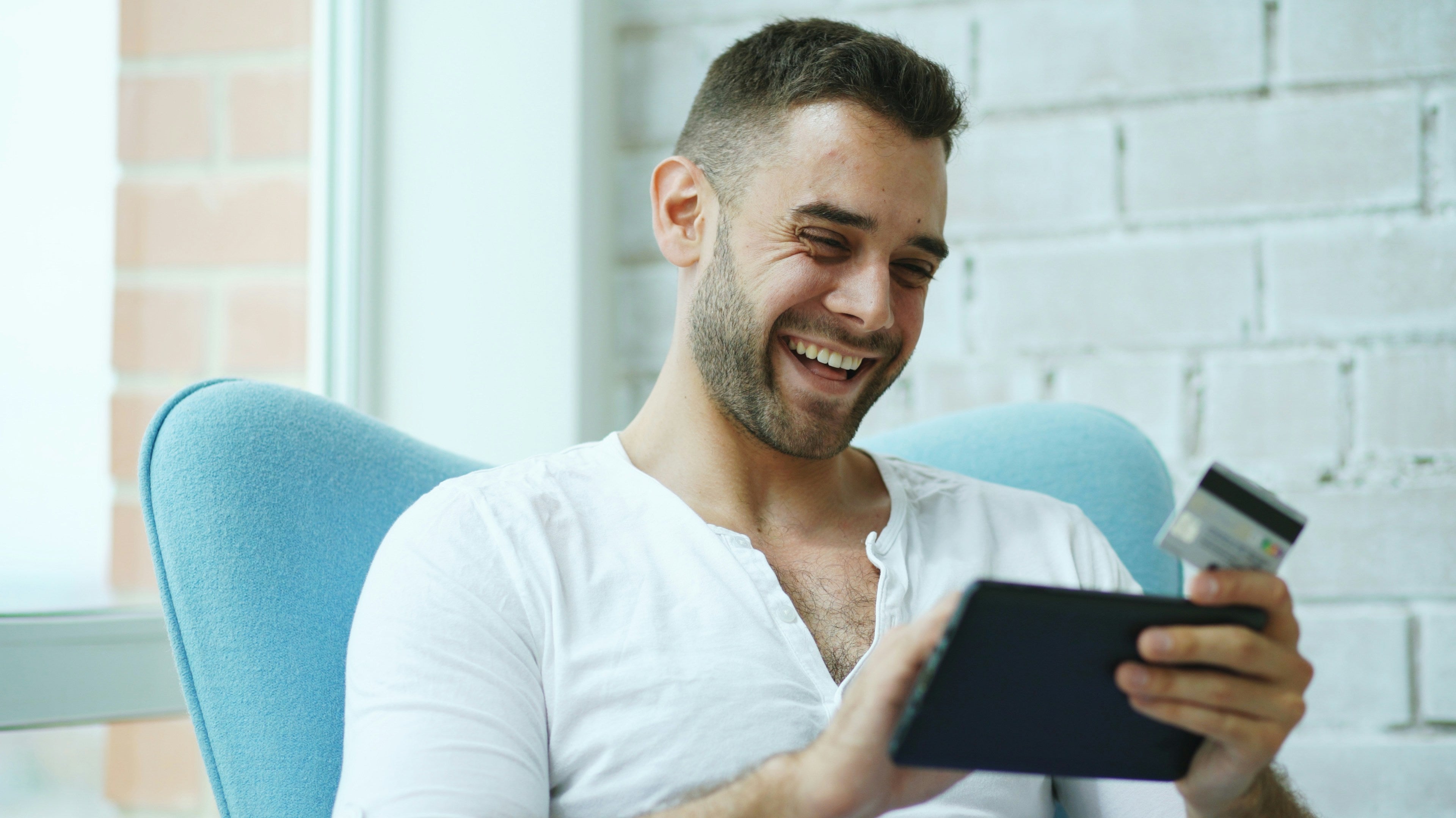 Man holding a tablet and credit card, smiling after making a purchase. 